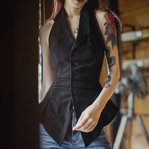 Person wearing a black vest with tattoos on arms indoors